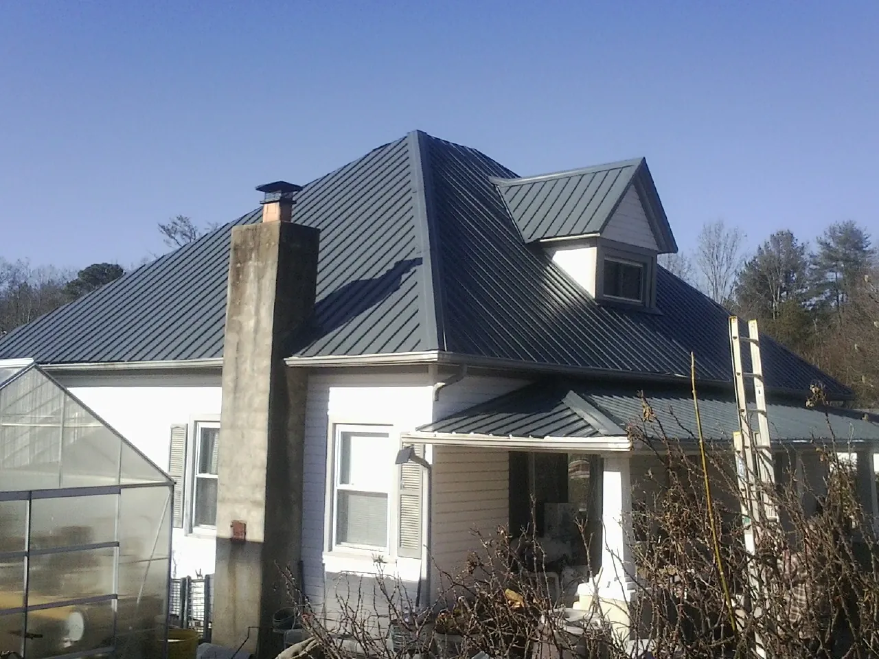 Dark blue standing seam metal roof on a white farmhouse with dormer — Slate & Tile Roof Repair by Roofing Brothers in Hot Springs Village