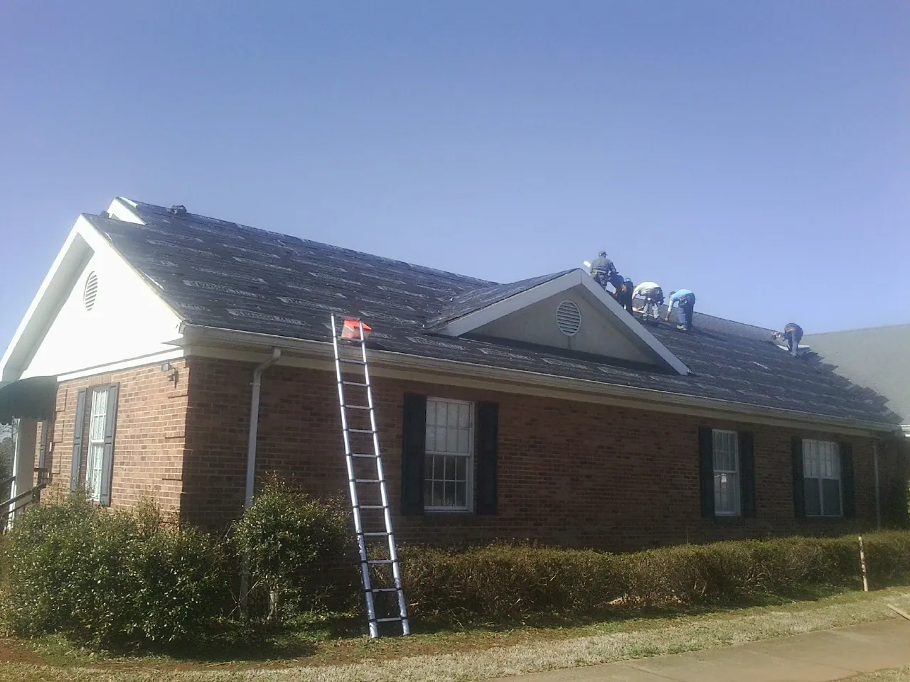 Crew tearing shingles off a brick ranch roof with a ladder set — Emergency Roof Repair work by our crew in Hot Springs Village