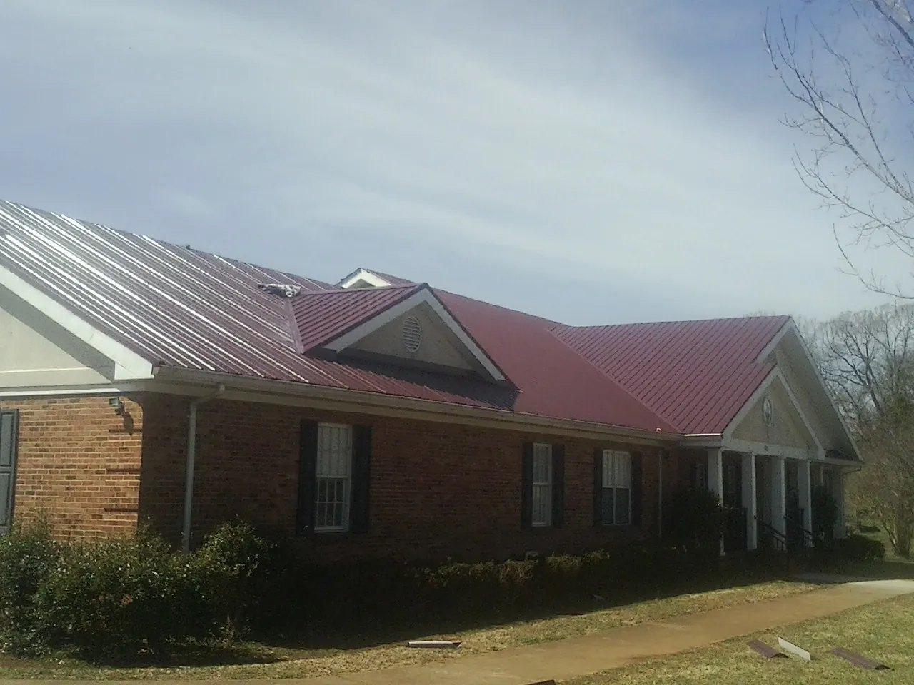 Red metal roof with gabled entries on a long brick building, from a Hail Damage Roof Repair job in Hot Springs Village