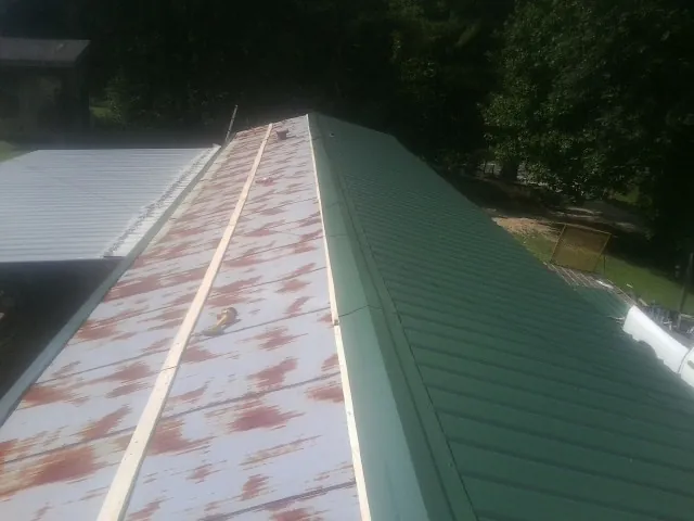 Old rusted panels beside newly installed green metal roofing — Wind Damage Roof Repair by Roofing Brothers in Hot Springs Village