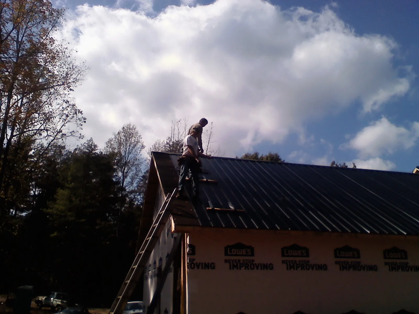Roofer fastening dark metal panels high against a cloudy sky, from a Roof Inspection job in Hot Springs Village