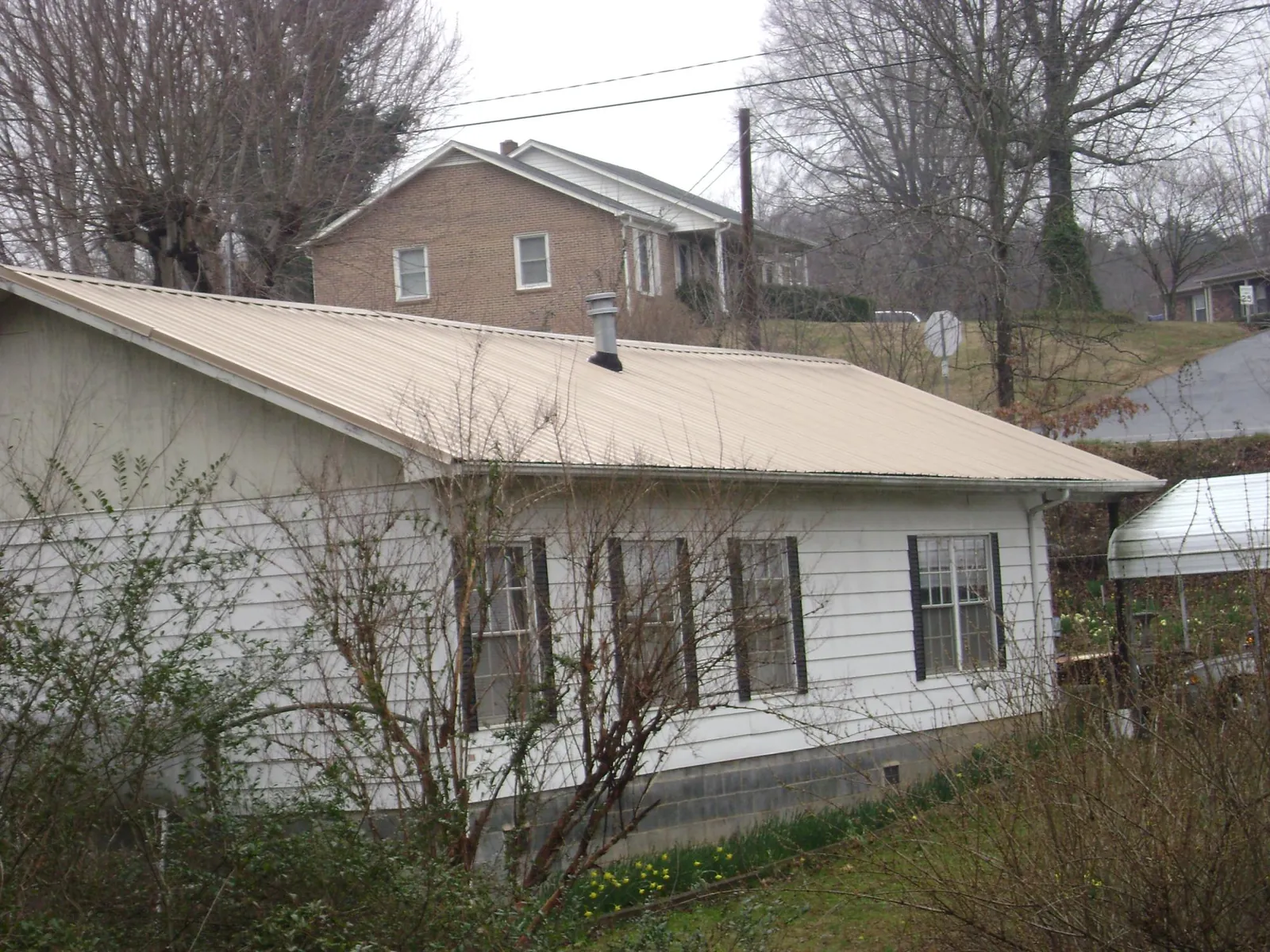 Tan metal roof on a white sided house set into a hillside — Commercial Roofing by Roofing Brothers in Hot Springs Village
